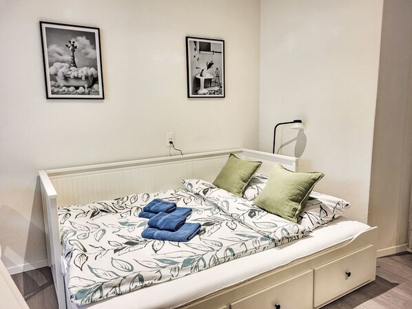 A bedroom with a bed, pillows, a bedside table, a lamp, and two framed pictures on the wall.