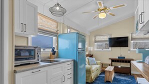 Una cocina compacta con armarios blancos, un refrigerador azul, un microondas y un ventilador de techo.