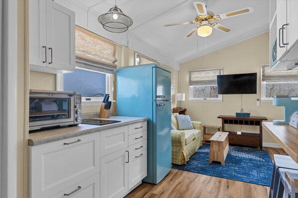 A compact kitchen with white cabinets, a blue refrigerator, a microwave, and a ceiling fan.