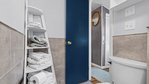 Un baño con un inodoro blanco, una puerta azul y un perchero con toallas dobladas.