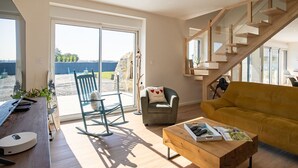 Een moderne woonkamer met een houten trap, een bank, een schommelstoel en een salontafel.