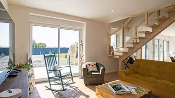 A modern living room with a wooden staircase, a sofa, a rocking chair, and a coffee table.