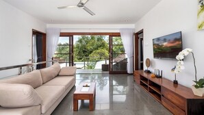Ein modernes Wohnzimmer mit einem beigefarbenen Sofa, einem Holztisch, einem an der Wand befestigten Fernseher und einem Balkon mit Glastüren.