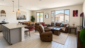 A spacious living area with a large sofa set, a dining area with chairs and a table, and a kitchen with a central island.