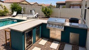 An outdoor kitchen area with a grill, a built-in oven, and a poolside lounge.