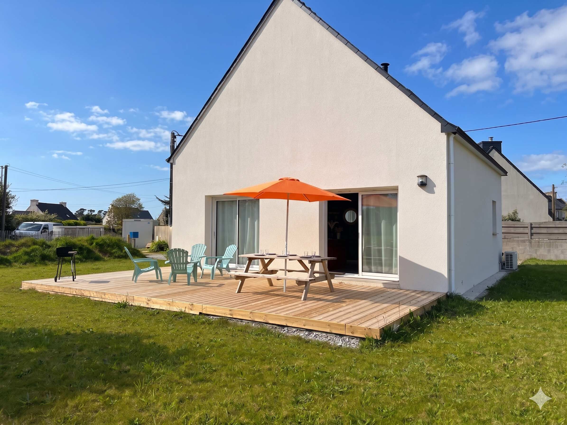 A small, single-story house with a wooden deck, a patio table, and chairs.