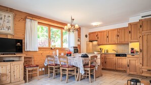 Eine gemütliche Küche mit Holzschränken, einem Esstisch mit Stühlen, einem Fernseher und einem Fenster mit Vorhängen.