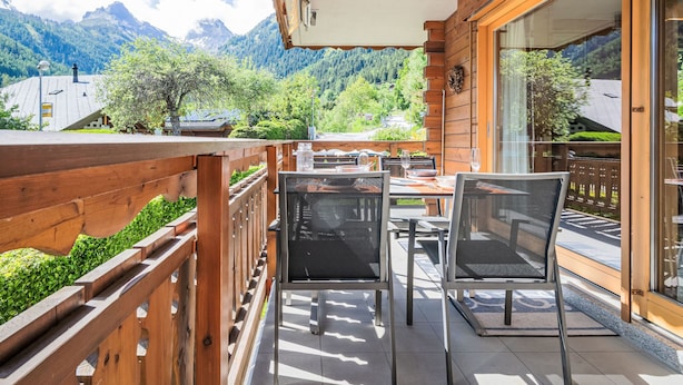 Ein Holzbalkon mit Tischen und Stühlen mit Blick auf eine gebirgige Landschaft.