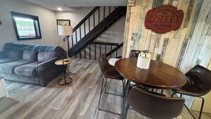 A cozy living room with a sofa, a coffee table, and a dining area with chairs. There's a staircase leading to another level.