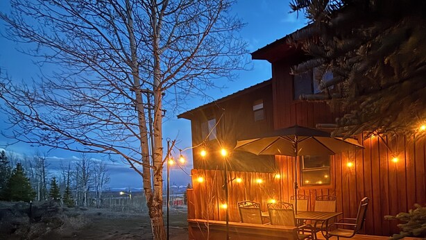 A wooden cabin with a deck, outdoor seating, and string lights.