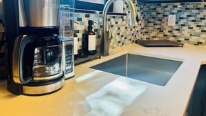A kitchen with a coffee maker, a sink, and a tiled backsplash.