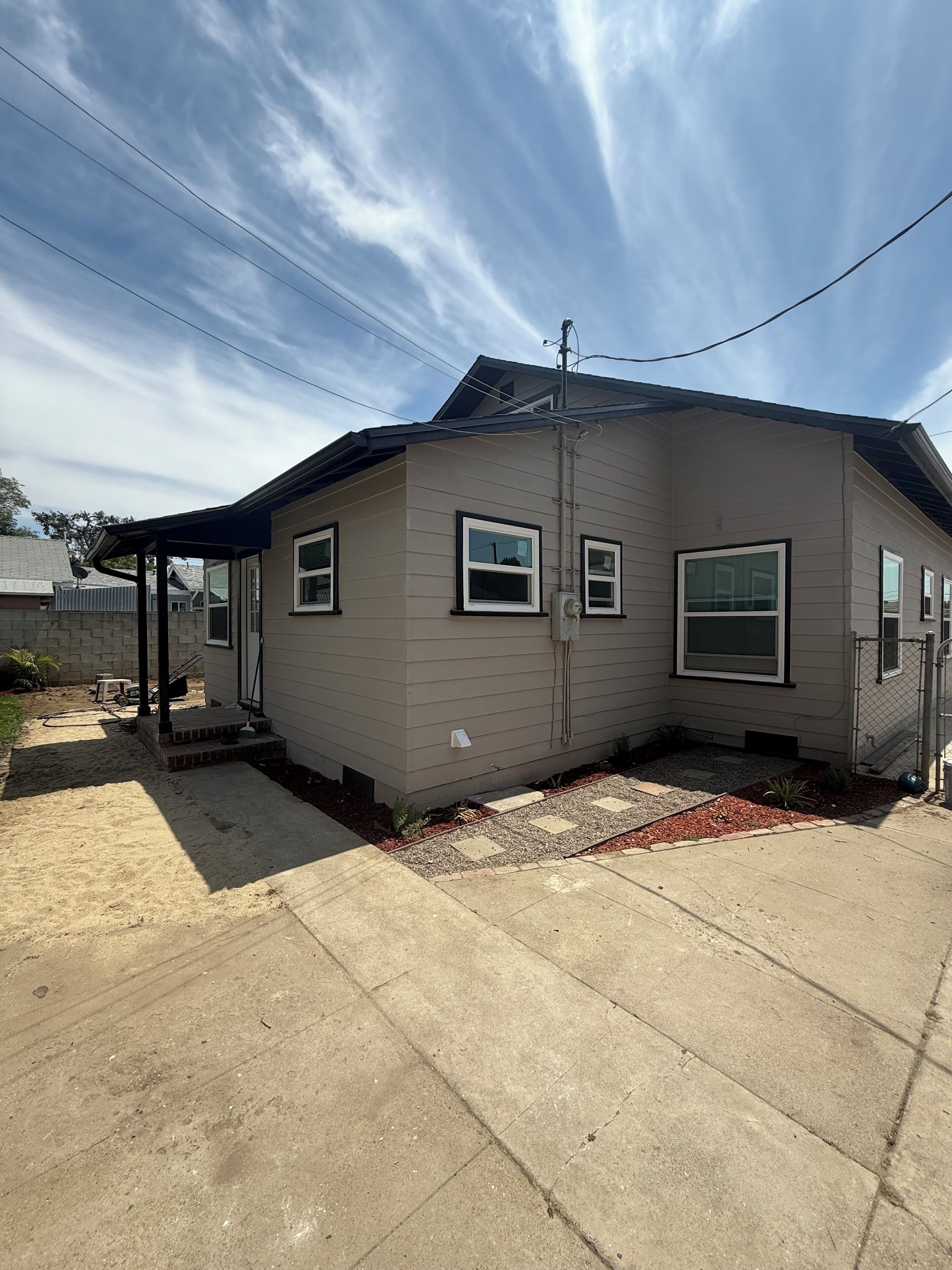 A single-story house with a covered porch, a fenced yard, and a clear sky.