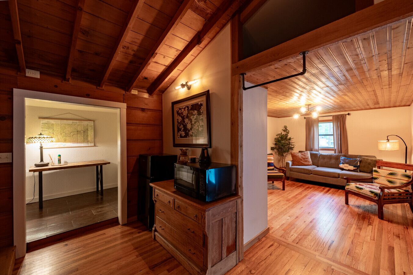 A wooden interior with a dining area, a living room with a sofa, and a kitchen area with a microwave.