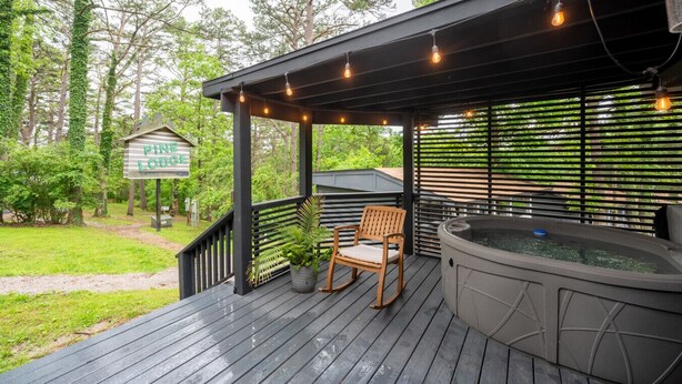 Terraza de madera con jacuzzi, sillas y luces colgantes. Se ve un cartel de Pine Lodge.
