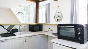 Eine kompakte Küche mit weißen Schränken, einer Bosch-Mikrowelle, einem Bosch-Toaster, einem Spülbecken und einem hängenden Spiegel.