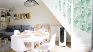 Ein modernes Wohnzimmer mit einem weißen Esstisch, weißen Stühlen, einem grauen Sofa und einer schwarzen Pendelleuchte.