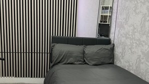 Ein modernes Schlafzimmer mit Bett, grauer Bettwäsche, einem großen Spiegel und einer Heizung.