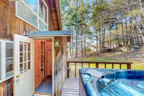 A wooden cabin with a hot tub, a deck, and a view of trees.