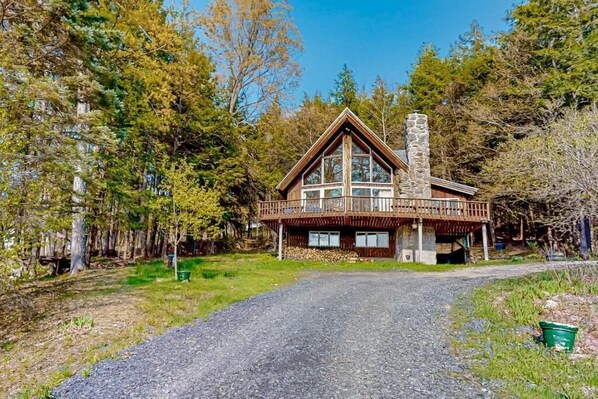 A cabin with a stone chimney, wooden exterior, and a balcony overlooking a forested area.