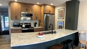 Una cocina con gabinetes de madera, un refrigerador de acero inoxidable, una encimera de granito y un tazón de frutas.