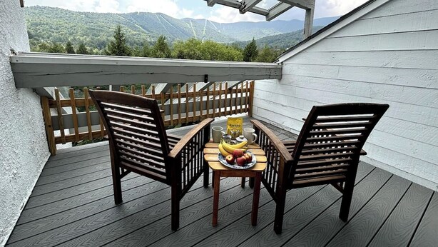 Una terraza de madera con dos sillas y una mesa, una bolsa de papas y un plato de fruta.