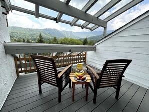 A wooden deck with two chairs and a table, a bag of chips, and a plate of fruit. - Bridges Resort Mountain Views of Sugarbush (Warren)