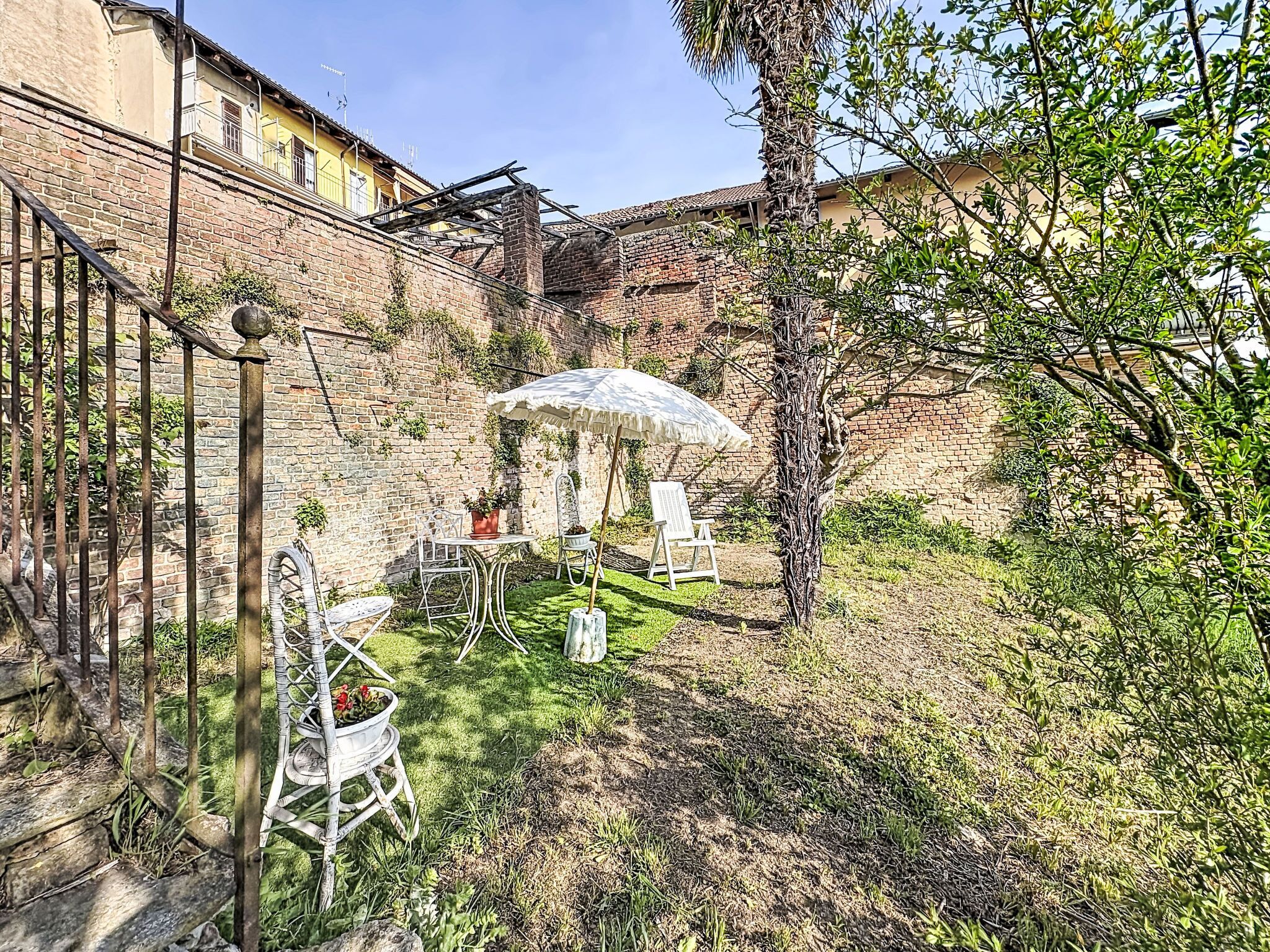 A courtyard with a brick wall, a white umbrella, and outdoor furniture.