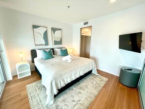 A modern bedroom with a bed, bedside tables, a TV, and artwork on the wall. - Q Tower - Deluxe Ocean View Apartment with King Bed & Spa (Surfers Paradise)