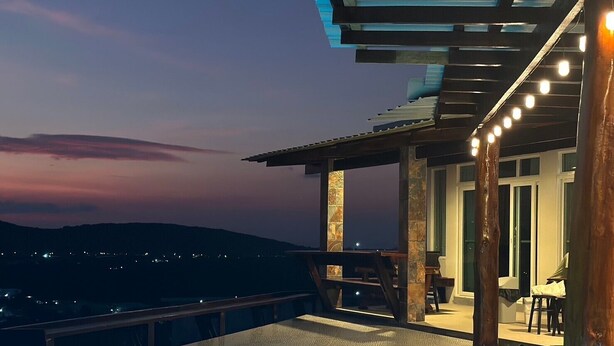 A rooftop pool with a geometric design, a dining area with outdoor seating, and a view of the cityscape at dusk.