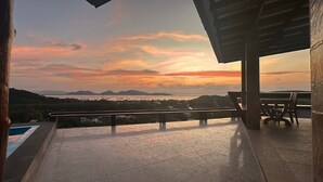 A balcony with a view of a sunset over a body of water and mountains.