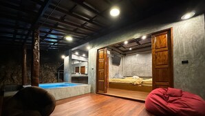 A room with a wooden floor, a small pool, a bed with a teddy bear, and a red bean bag.