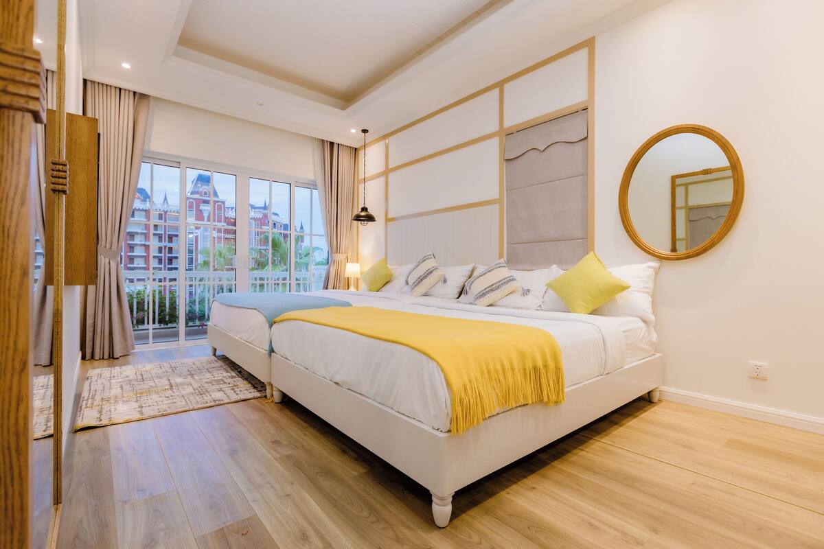 Ein Schlafzimmer mit einem großen Bett, Blick auf ein Gebäude durch eine Glastür und einem Spiegel an der Wand.