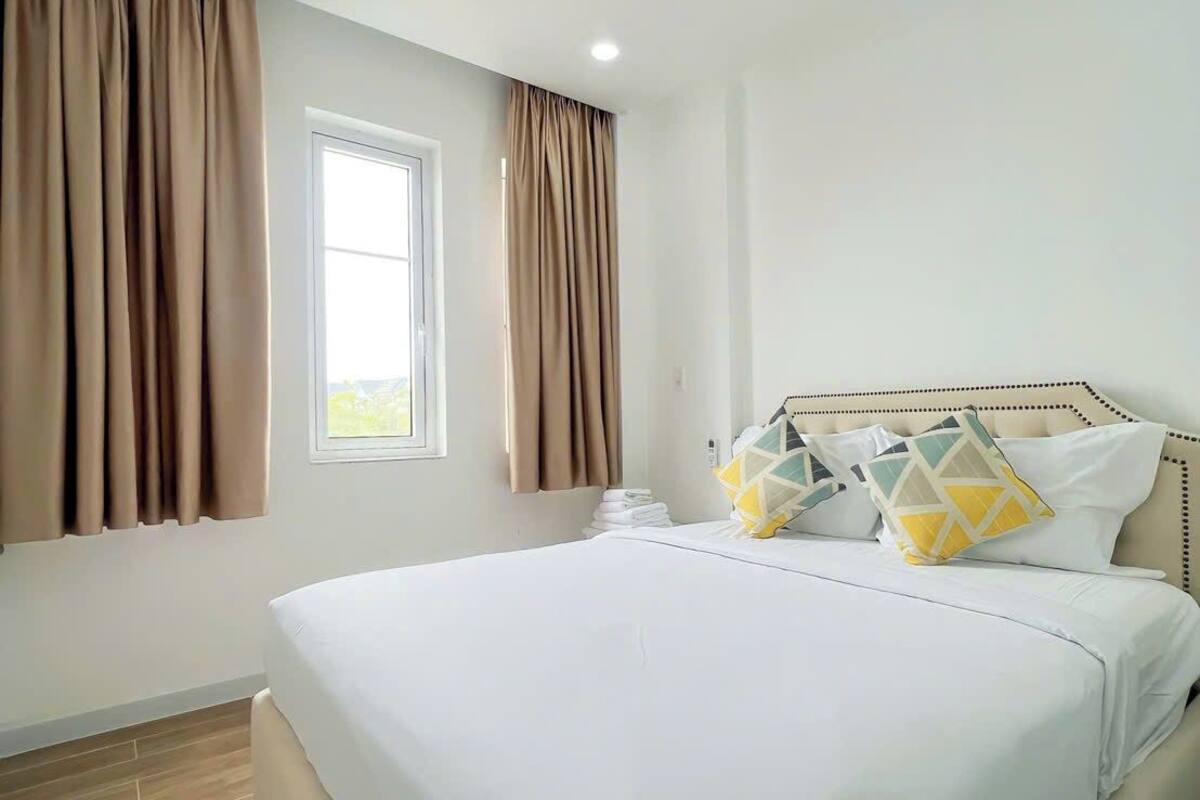 Ein Hotelzimmer mit einem großen Bett, beigen Vorhängen, einem Fenster und einem Kopfteil mit gemusterten Kissen.