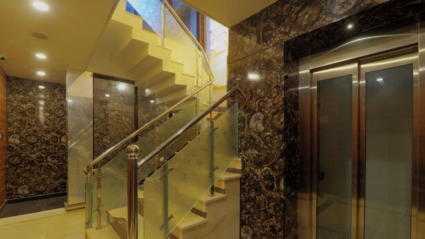 Een modern interieur met een marmeren trap, een glazen lift en uitzicht op de lucht.