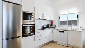 A modern kitchen with stainless steel appliances, white cabinetry, and a window with a stone wall view.