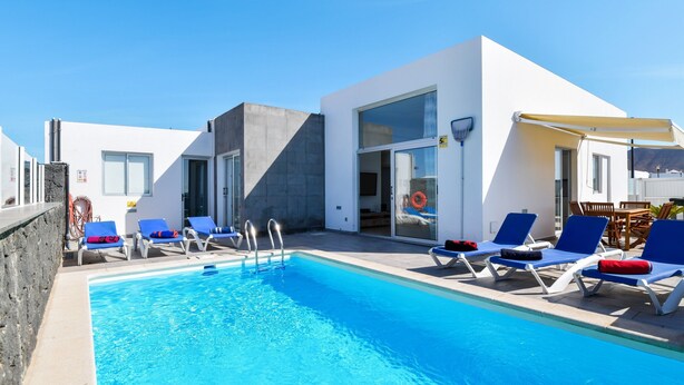 A modern pool area with blue lounge chairs and a clear blue pool.