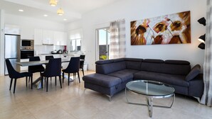A modern living area with a sofa, dining table, chairs, kitchen, and artwork.