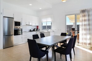 Een moderne keuken met witte kasten, een roestvrijstalen koelkast, een inbouwoven en een eethoek met een tafel en stoelen.