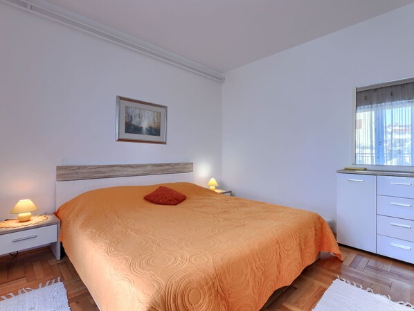 A bedroom with a large bed, a bedside table with a lamp, a dresser, and a window with a view.