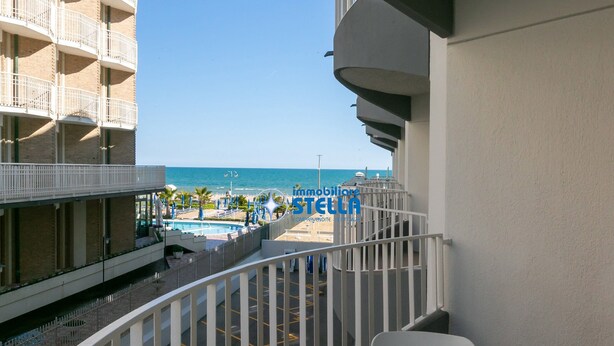 Un balcone con vista su una piscina e una spiaggia, una ringhiera bianca e un edificio con balconi.