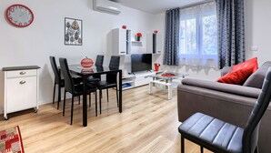 A modern living room with a sofa, a dining table with chairs, a TV, and a white cabinet.