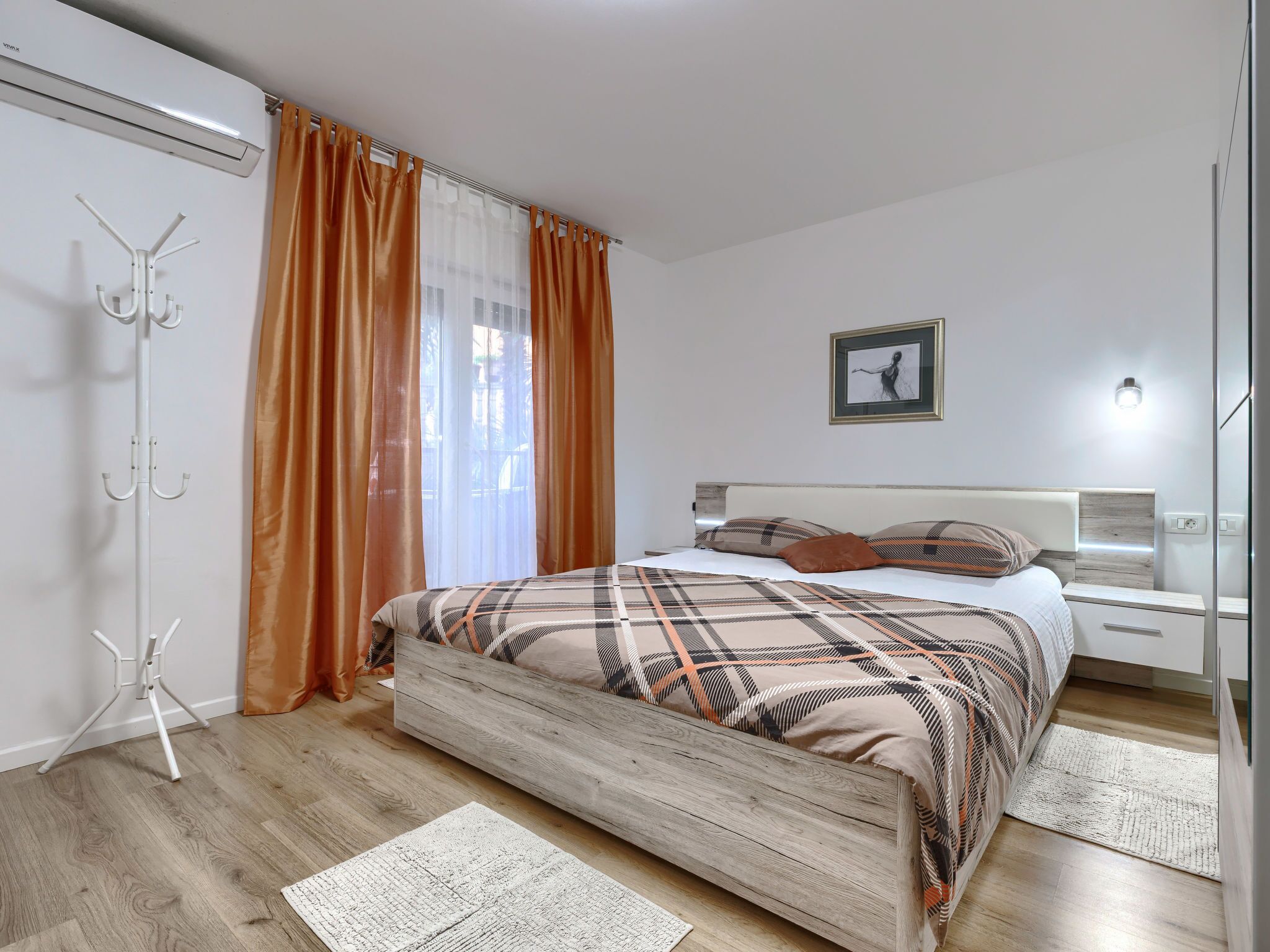 Una camera da letto moderna con un letto in legno, un appendiabiti e un'ampia finestra con tende.