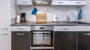 A modern kitchen with white cabinets, a stainless steel range hood, a built-in oven, a coffee maker, a kettle, and a sink with a marble backsplash.