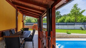 Eine überdachte Terrasse mit Pool, Holzmöbeln und Blick auf eine grüne Rasenfläche.