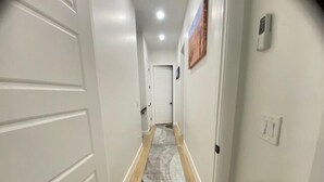A hallway with white walls, a gray and black rug, and a wooden floor. - Modern Mountain Escape | Cozy Retreat with Stunning Views (Eden)
