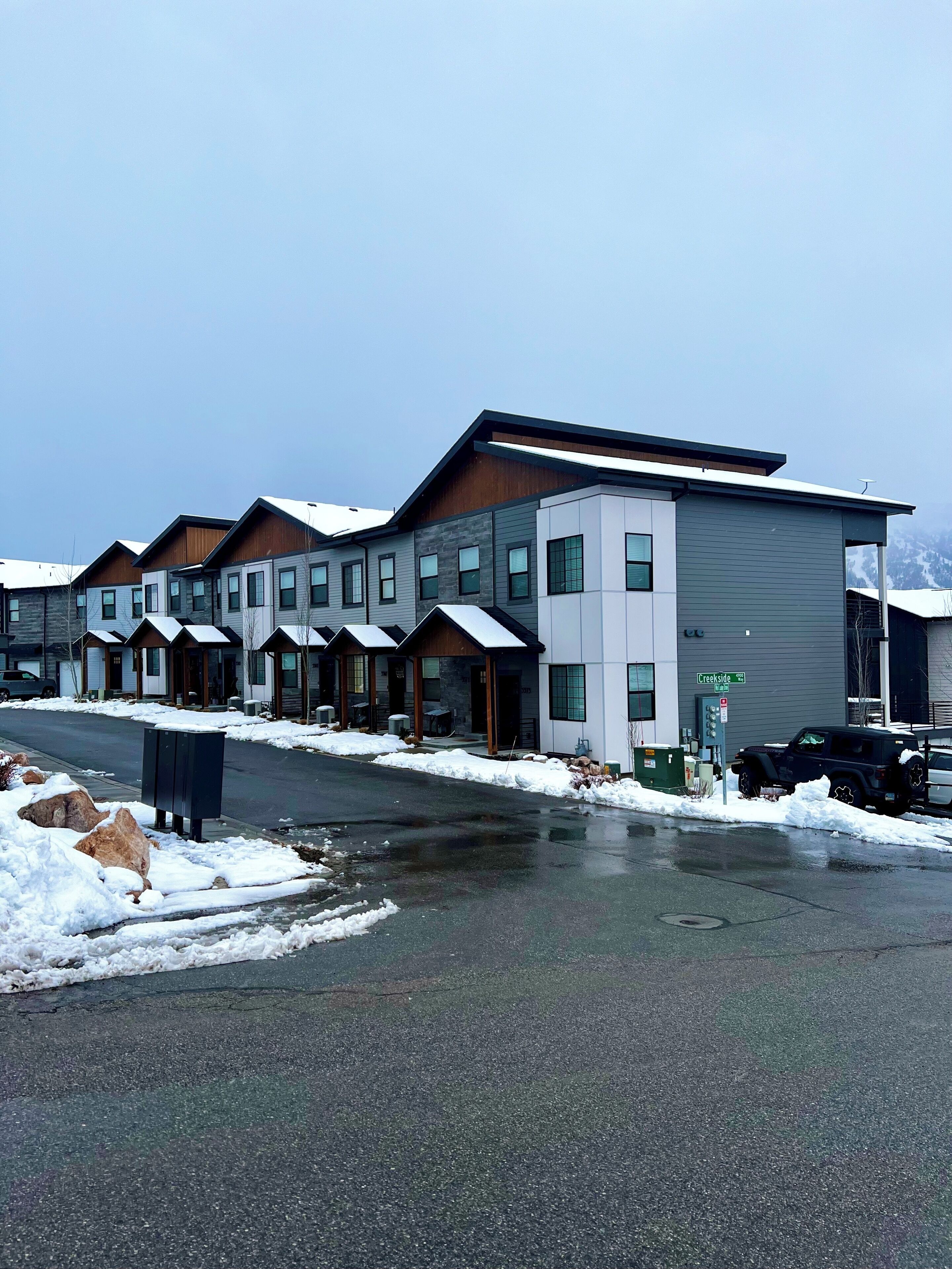 Un edificio moderno con diverse unità, una zona esterna coperta e un parcheggio innevato.
