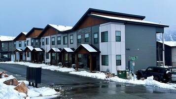 Un edificio moderno con diverse unità, una zona esterna coperta e un parcheggio innevato.