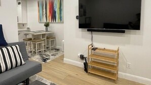 A modern living room with a flat-screen TV mounted on the wall, a grey sofa with striped cushions, a wooden coffee table, and a colorful abstract painting on the wall. - Modern Mountain Escape | Cozy Retreat with Stunning Views (Eden)
