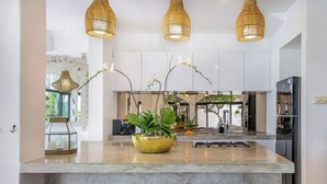 A modern kitchen with a central island, bar stools, and hanging wicker pendant lights. - Homey 5 BR Villa In Seminyak (Seminyak)