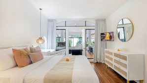 A modern hotel room with a large bed, a TV, a dresser, and a balcony with a view. - Homey 5 BR Villa In Seminyak (Seminyak)